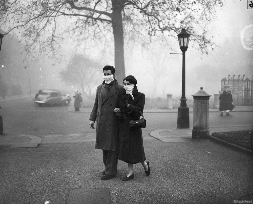 November 1953:  A couple walking in London wearing smog masks on a foggy day.  (Photo by Monty Fresco/Topical Press Agency/Getty Images)