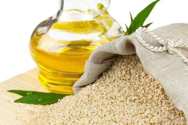 Macro view of sesame seeds in flax sack and glass bottle of sesame oil on mat isolated on white background