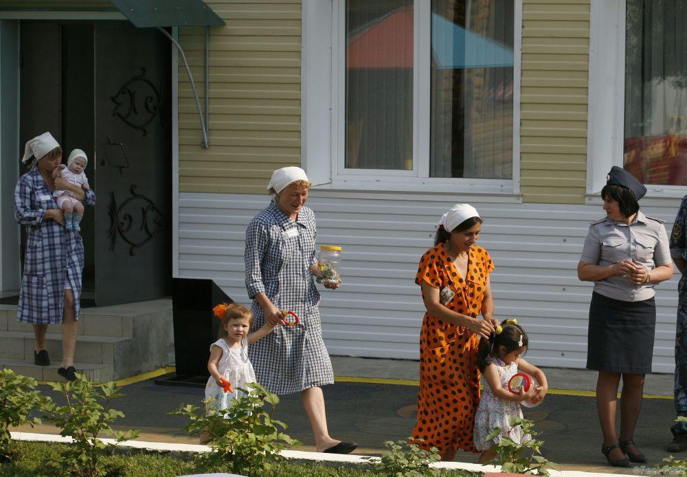 Inmates walk with their children as a guard (R) watches in the courtyard of a "children's home" located inside a female prison camp, in Russia's Siberian city of Krasnoyarsk, July 30, 2012. The children of female offenders that were born when their mothers were in pretrial detention or in prison camps, live in the "children's home" under the care of civilian tutors and officers of the regional penitentiary system up till the age of about 3-year-old, after which they are released to their relatives or sent to a civilian orphanage. The mothers also receive exemption from some of their usual duties and tasks in order to have daily contact with their children, according to the camp's administration. REUTERS/Ilya Naymushin (RUSSIA  - Tags: SOCIETY CRIME LAW) - RTR35MGO