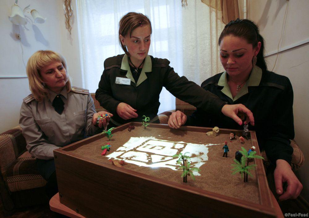 A prison psychologist (L) looks on as two inmates create a sand drawing inside female prison camp Number 22 in Russia's Siberian city of Krasnoyarsk, November 21, 2013. Inmates in the prison are offered the opportunity to draw with sand as an experimental form of therapy, prison authorities said.  REUTERS/Ilya Naymushin (RUSSIA - Tags: CRIME LAW) - RTX15N9E