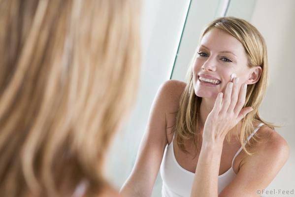 Woman in bathroom applying face cream smiling