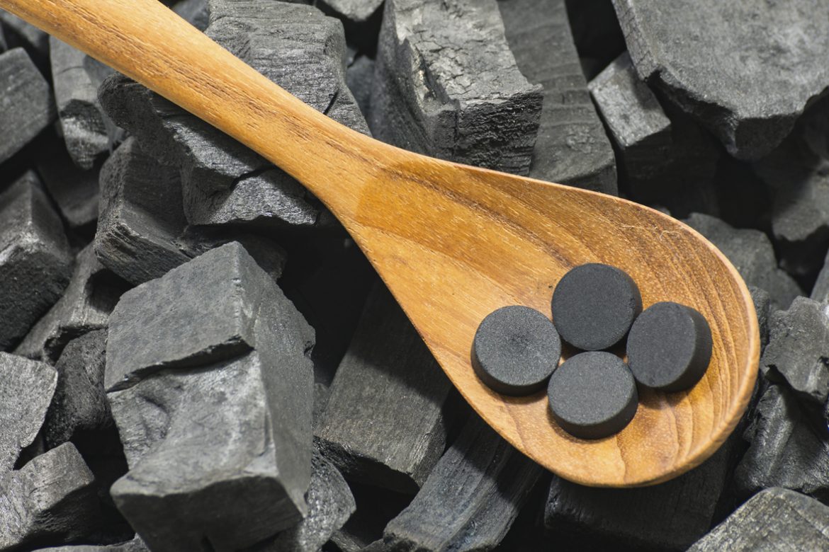 activated carbon pill in wood spoon on charcoal texture background