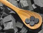 activated carbon pill in wood spoon on charcoal texture background