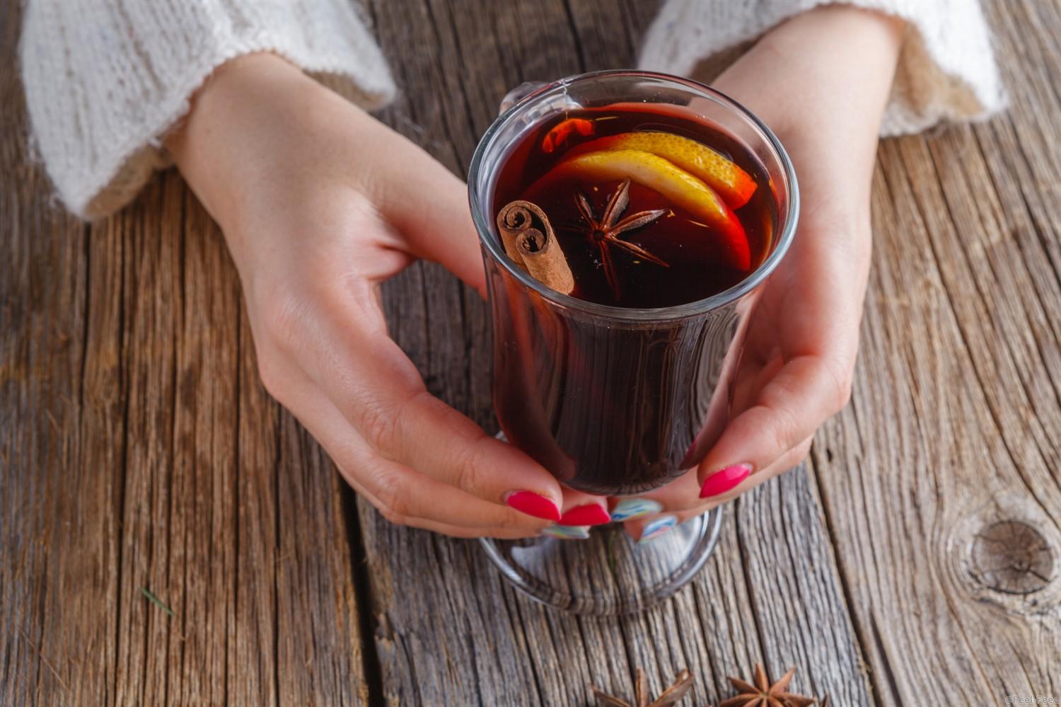 Hot mulled wine in female hands, spices on weathered wooden table. Sweet home concept