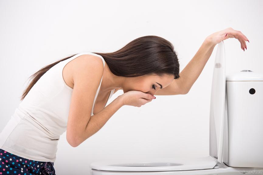 Young woman vomiting into the toilet bowl in the early stages of pregnancy or after a night of partying and drinking.