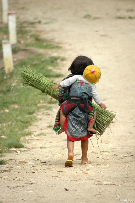 A tiny H'mong girl carrying her baby brother and a bundle of reeds across a valley in Sapa, Vietnam. She couldn't have been older than 4 years, but already she was hard at work helping her family.