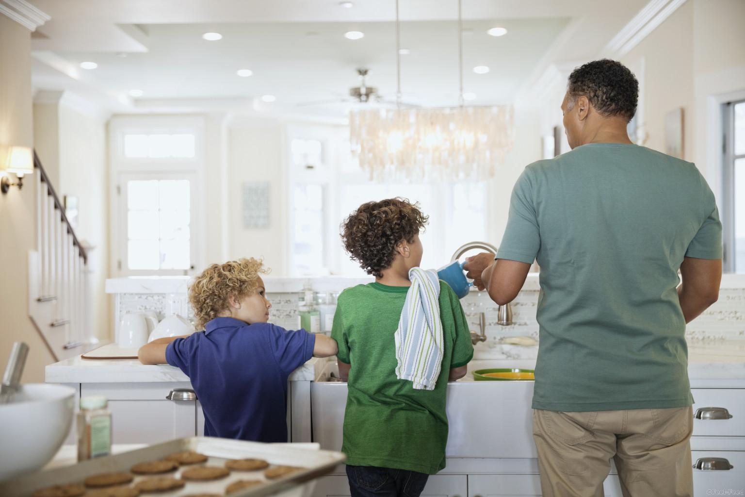 Rear view of children and father washing dishes at kitchen sink
