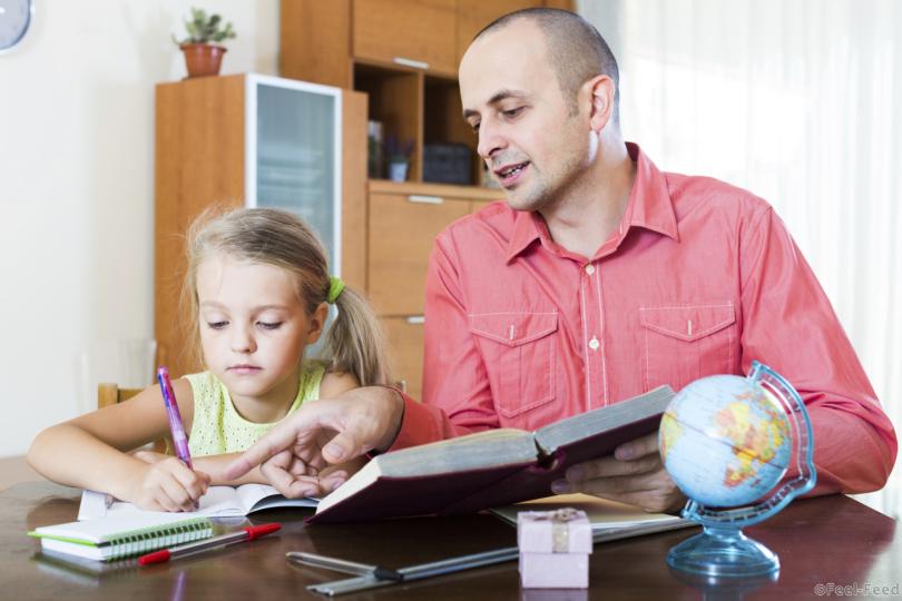 Portrait of positive european dad helping schoolgirl to study at home