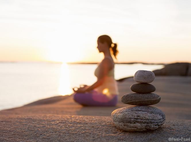 Side view of woman sitting in lotus position on lakeshore with focus on stack of stones